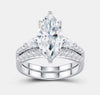 Marquise moissanite ring set resting on white stone surface — lifestyle product photo showing stacked engagement and wedding band