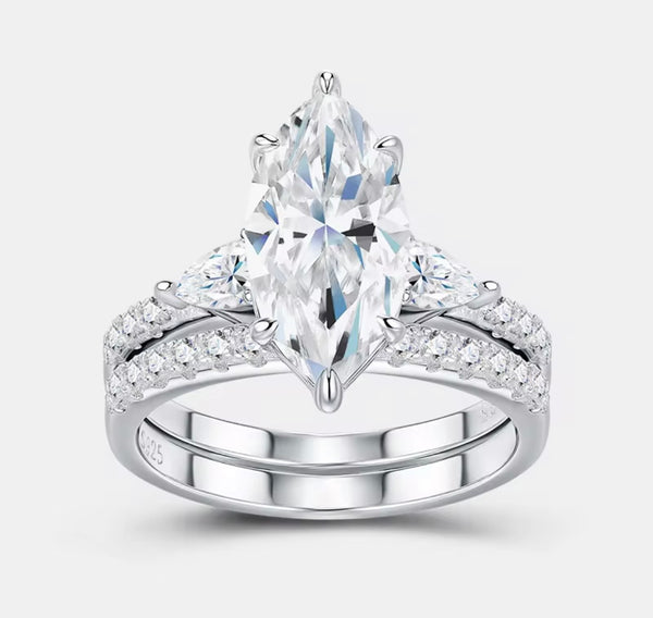 Marquise moissanite ring set resting on white stone surface — lifestyle product photo showing stacked engagement and wedding band