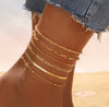 6 piece 14K gold stacked anklet set displayed on ankle — snake, figaro, paperclip, box, rope, and satellite chain styles