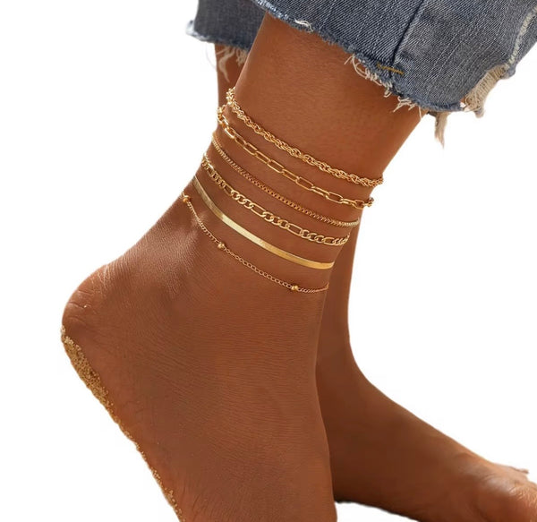 6 piece 14K gold stacked anklet set displayed on ankle — snake, figaro, paperclip, box, rope, and satellite chain styles