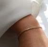 A delicate gold chain bracelet worn on a person's wrist, shown in a close-up shot with a soft white sleeve in the background.