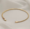 A gold-toned chain bracelet with a lobster clasp and a polished end tab, displayed on a soft white satin fabric background.