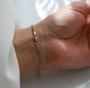 A delicate gold chain bracelet worn on a person's wrist, shown in a close-up shot with a white sleeve visible on the left.