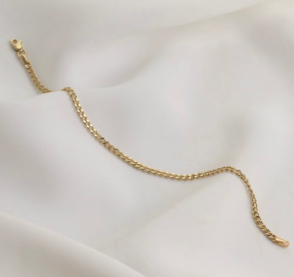 A gold chain bracelet with a lobster clasp, displayed on a draped white fabric background.
